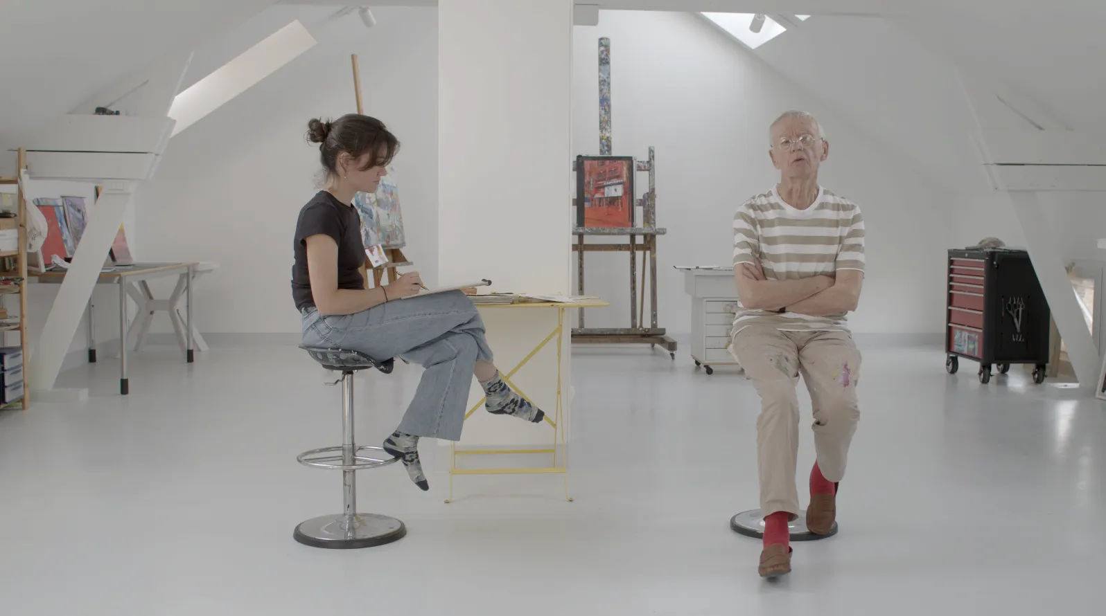 Camille Authouart assise sur un tabouret en train de dessiner à une petite table, son père debout à ses côtés dans le studio de tournage