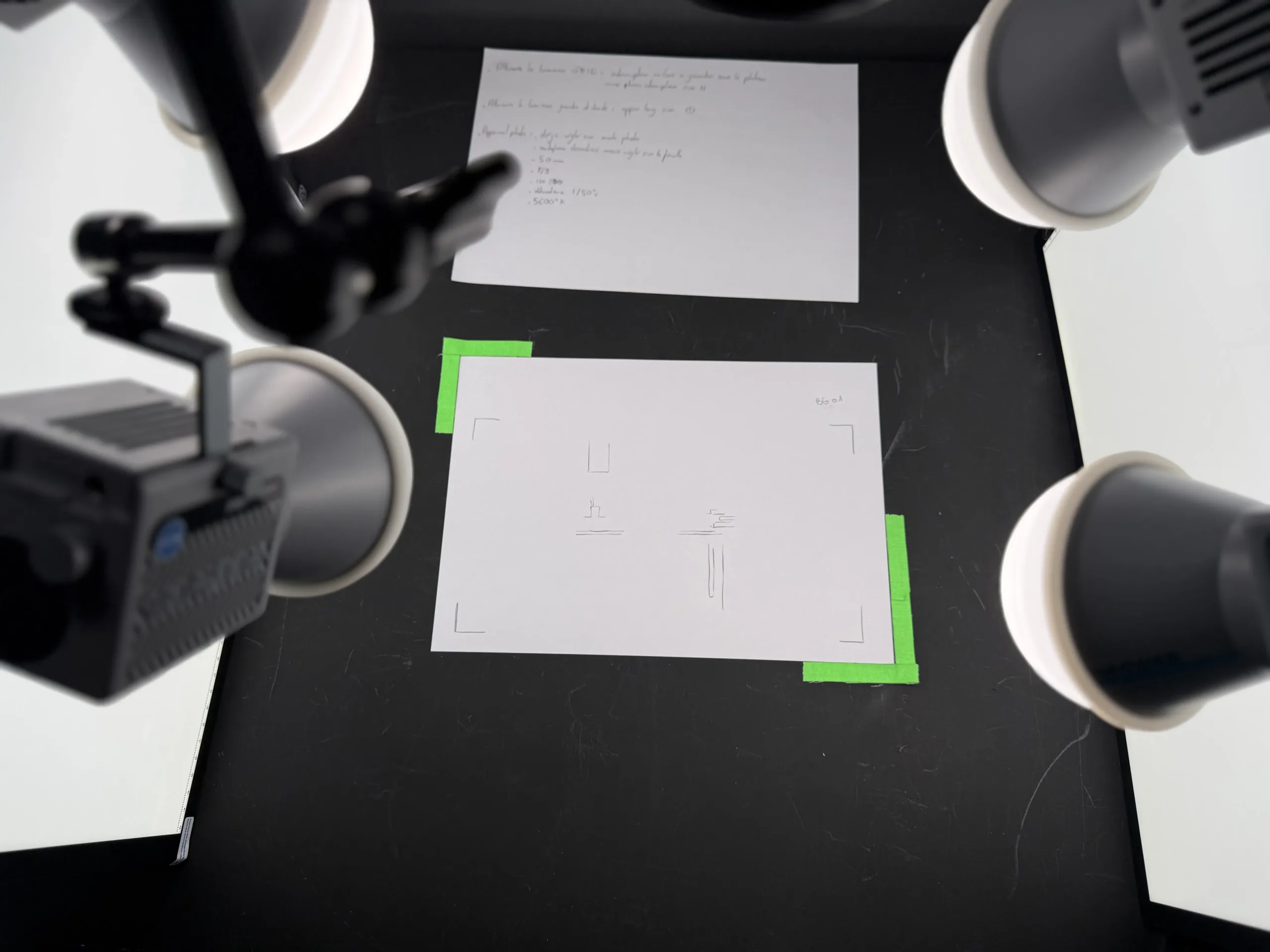 Dispositif de banc-titre : caméra montée sur bras articulé, éclairée par deux torches, photographiant des dessins posés sur une surface noire au Studio Amopix